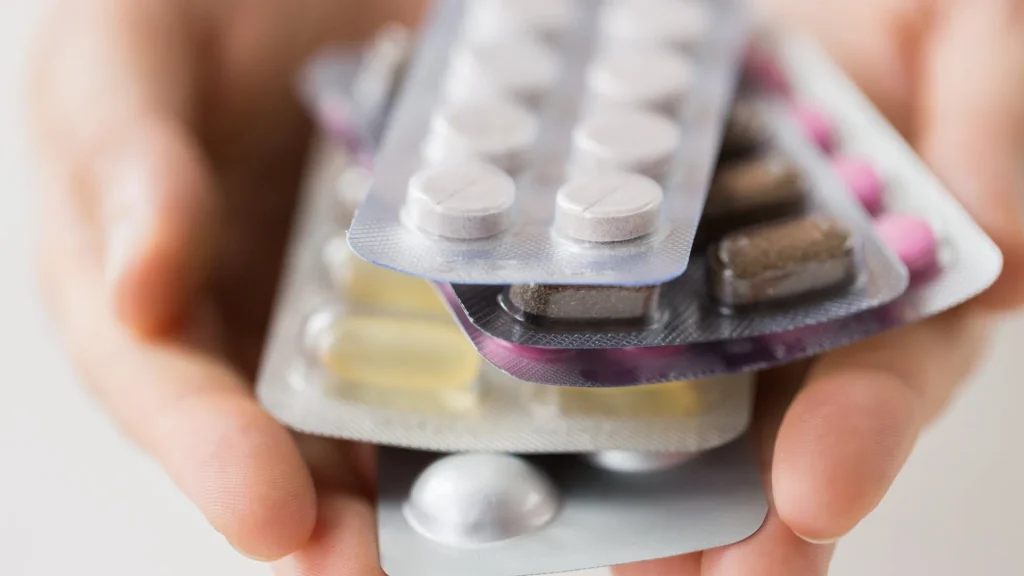 Manos sosteniendo varios blísteres de medicamentos, ejemplo de automedicación con antibióticos