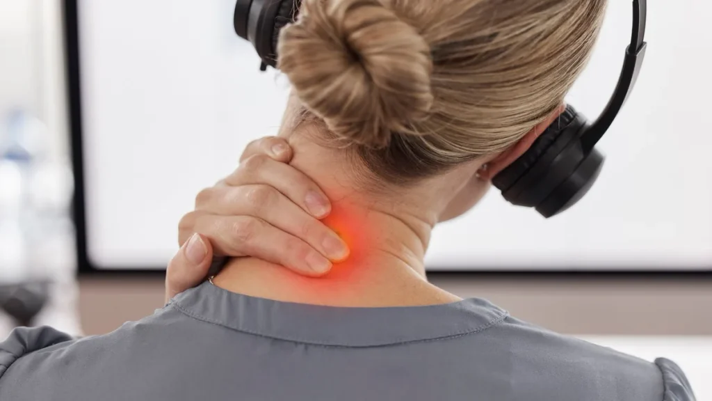Mujer con auriculares se toca el cuello dolorido en el trabajo y busca aliviar el dolor cervical urgente