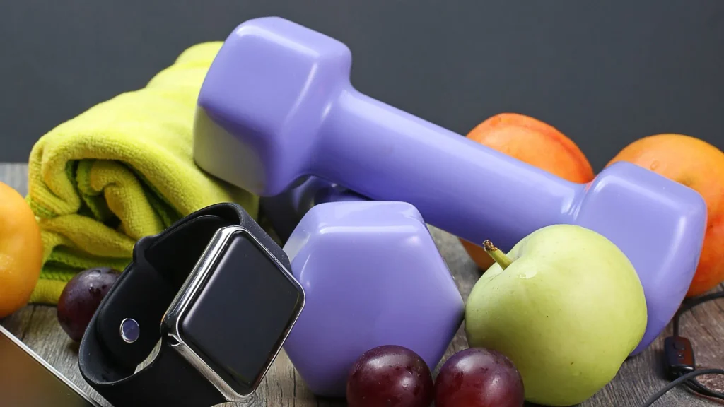 Mancuernas moradas junto a fruta y auriculares para una rutina de ejercicio y alimentación saludable