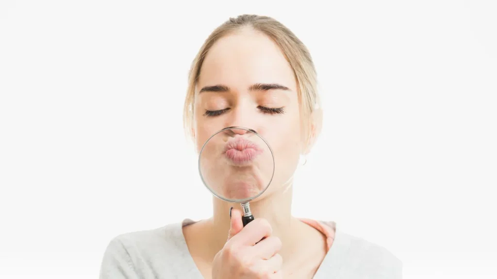Mujer que observa sus labios con una lupa para detectar los primeros síntomas del brote
