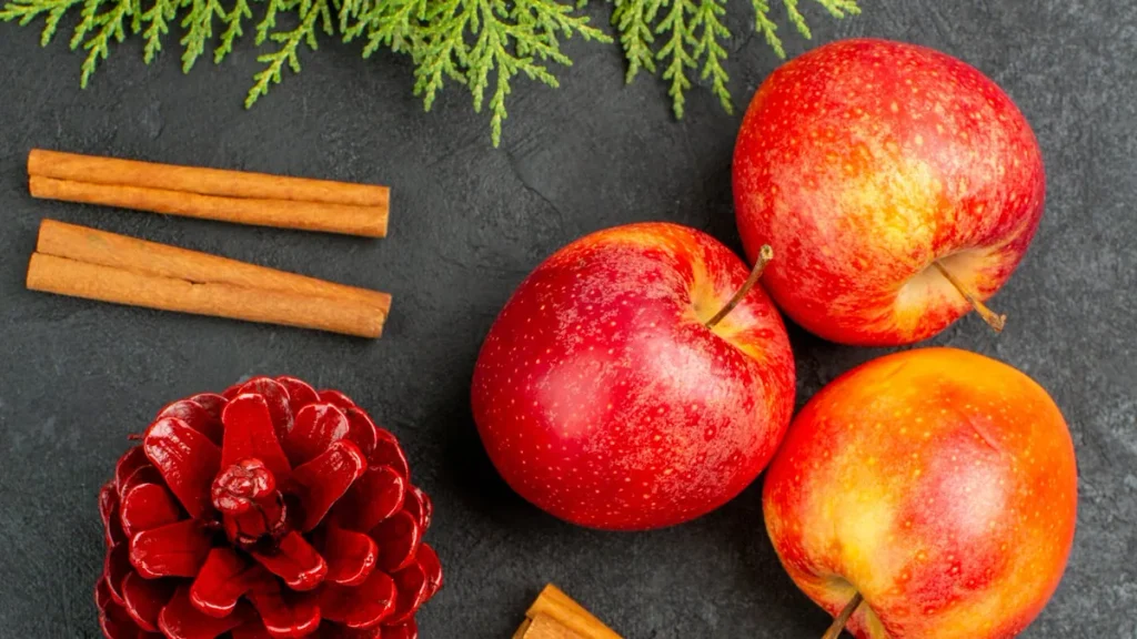Manzanas frescas, canela en rama y piñas decorativas sobre una mesa oscura