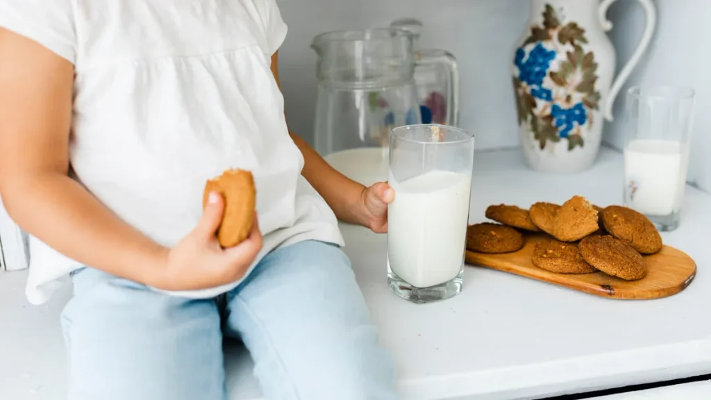 Niño sentado con una galleta en la mano junto a un vaso de leche y un plato de galletas
