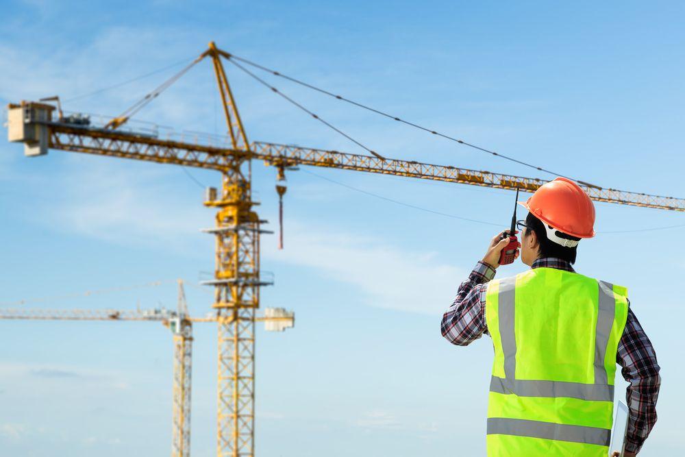 Trabajador con casco y equipo de seguridad junto a una grúa en una obra